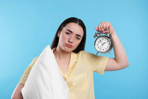 薄い青の背景に枕と目覚まし時計を持つ疲れた若い女性 不眠症の問題 — ストック写真