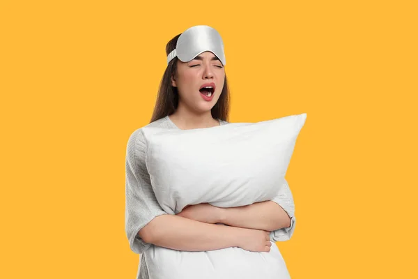 黄色の背景に睡眠マスクと枕のあくびをして疲れた若い女性 不眠症の問題 — ストック写真