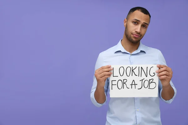 年轻的失业男子拿着写着 寻找紫色背景的工作 的标语 案文的篇幅 — 图库照片