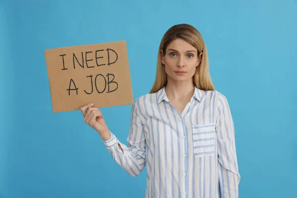 拿着标语牌的失业妇女我需要一份浅蓝色背景的工作 — 图库照片