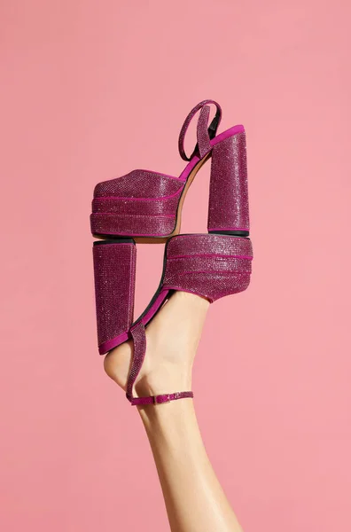 Woman wearing high heeled shoe with platform and square toes holding another one on pink background, closeup. Stylish presentation
