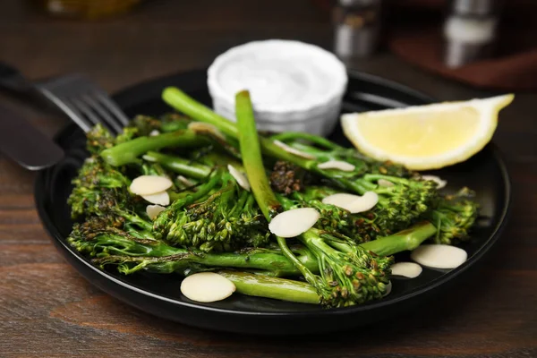 Stock image Tasty cooked broccolini with almonds, lemon and sauce on wooden table, closeup