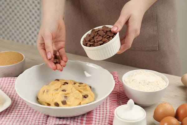 Cooking sweet cookies. Woman adding chocolate chips to dough at table in kitchen, closeup