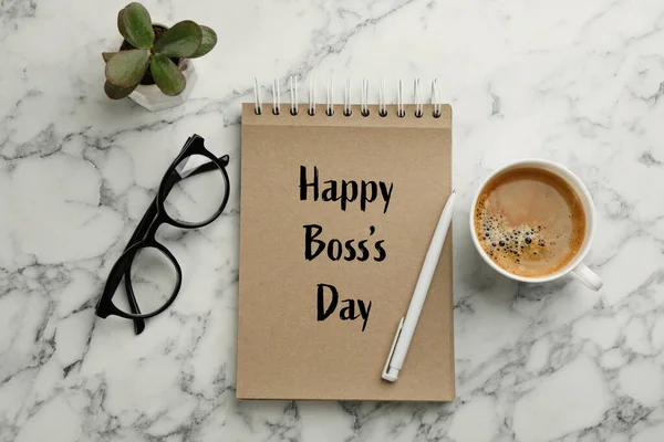 Notebook with phrase Happy Boss`s Day, coffee, glasses and plant on marble table, flat lay