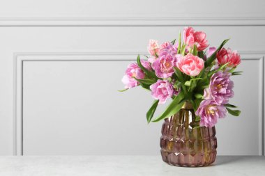 Açık gri duvarın yanındaki beyaz masada renkli lale çiçeklerinden oluşan güzel bir buket.