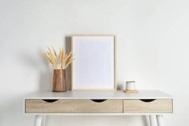 Boş fotoğraf çerçevesi, fincan ve vazo, beyaz masa üzerinde kuru dekoratif çiviler. Tasarım için model