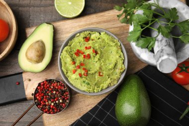 Bir kase lezzetli guacamole ve ahşap masada malzemeler.