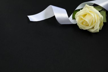 Siyah arka planda güzel bir gül ve beyaz kurdele, yazı için boşluk. Cenaze sembolleri