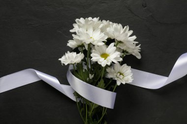 Güzel kasımpatı çiçekleri ve siyah masanın üstünde beyaz kurdele, üst manzara. Cenaze sembolleri