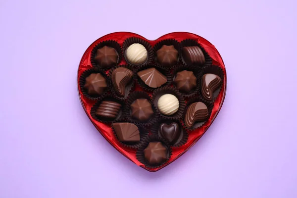 Hartvormige Doos Met Heerlijke Chocolade Snoepjes Lila Achtergrond Bovenaanzicht — Stockfoto