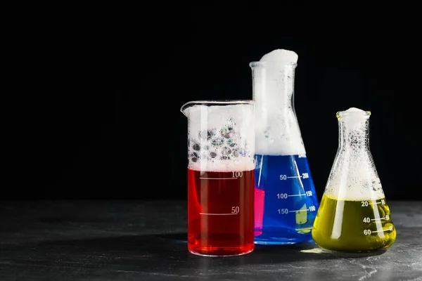 Laboratory glassware with colorful liquids on dark table against black background, space for text. Chemical reaction