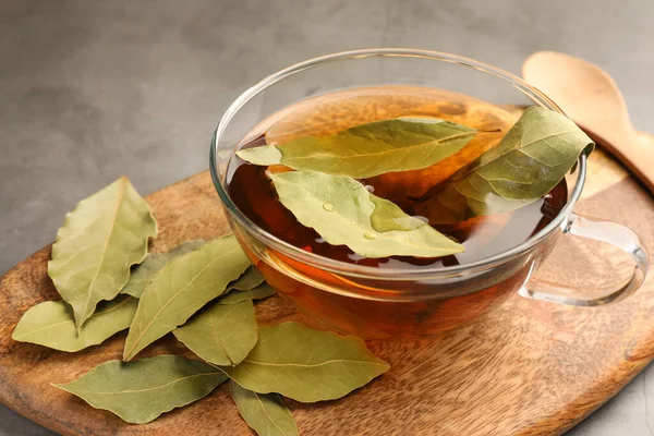 stock image Cup of freshly brewed tea with bay leaves on grey table, closeup