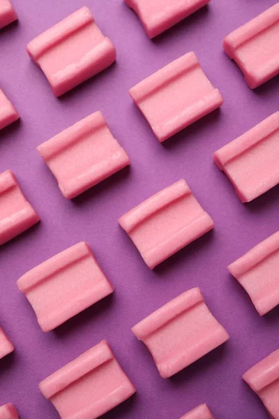 Tasty pink chewing gums on purple background, flat lay