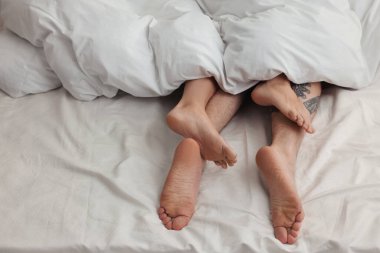 Tutkulu çift yatakta sevişiyor, bacakları birbirine yakın.