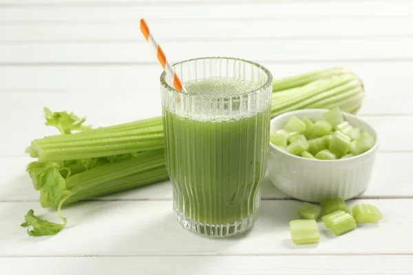 Glass of celery juice and fresh vegetables on white wooden table