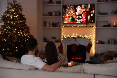 Çift, rahat bir odada televizyon izleyerek Noel filmi izliyor. Kış tatili atmosferi
