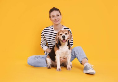 Turuncu arka planda sevimli Beagle köpeği olan mutlu genç bir kadın. Sevimli hayvan