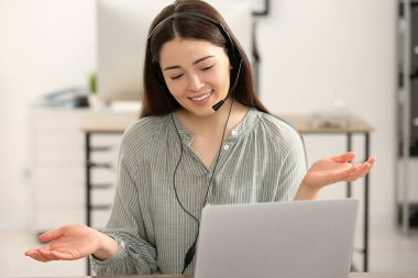 Ofiste dizüstü bilgisayarda çalışan kulaklıklı bir yardım hattı operatörü.