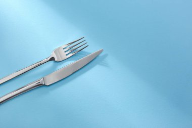 Açık mavi arka planda parlak çatal ve bıçak. Metin için boşluk