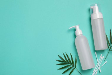 Farklı temizleyiciler, pamuk tomurcukları ve turkuaz arka planda yapraklar, metin için yeri olan düz bir yer. Kozmetik ürünü