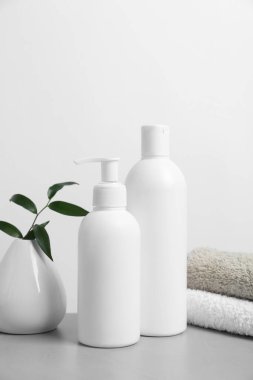 Farklı kozmetik ürünleri olan şişeler ve açık gri masa üzerindeki vazoda yeşil yapraklar beyaz arka planda