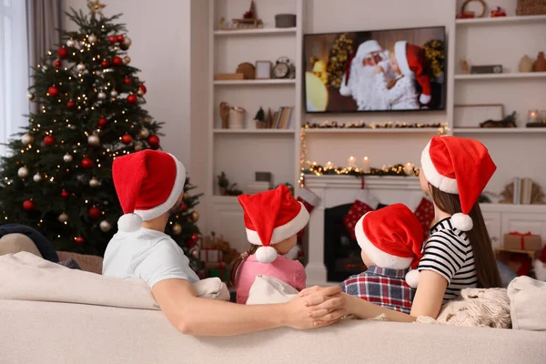 居心地の良い部屋でテレビを見てクリスマスの帽子をかぶっている家族 バックビュー 冬の休日の雰囲気 — ストック写真