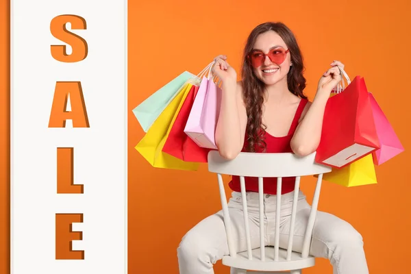 Happy woman in stylish sunglasses with many colorful shopping bags and word Sale on against orange background