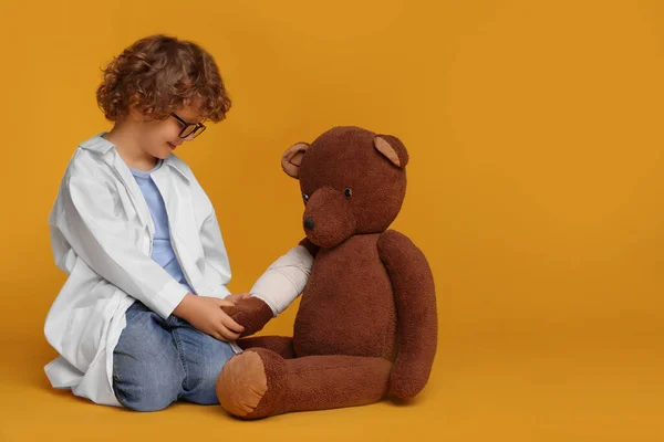 Mały Chłopiec Mundurze Medycznym Niedźwiedź Zabawka Bandażem Żółtym Tle Miejsce — Zdjęcie stockowe
