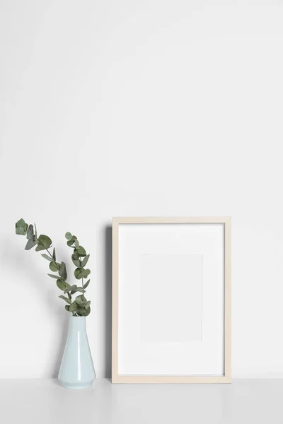白いテーブルの上に装飾的なユーカリの葉と空の写真フレームと花瓶 デザインのためのモックアップ — ストック写真