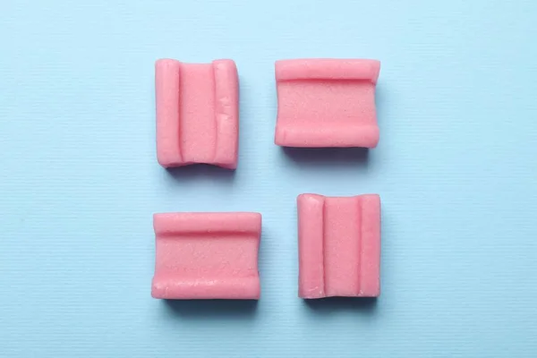 Tasty pink chewing gums on light blue background, flat lay