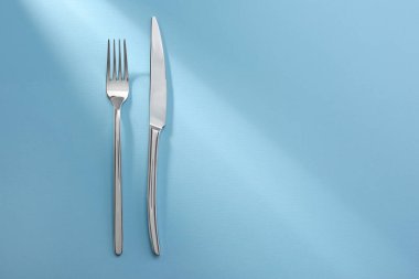 Açık mavi arka planda parlak çatal ve bıçak, düz yatıyordu. Metin için boşluk