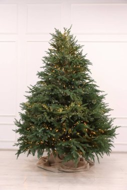 Beyaz duvarın yanında süslü ışıklarla süslenmiş güzel Noel ağacı