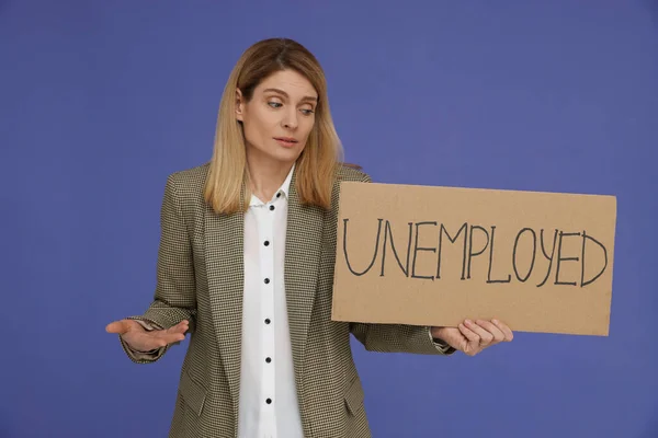 Confused woman holding sign with word Unemployed on violet background