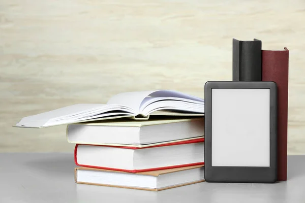 Portable e-book reader and many hardcover books on white textured table