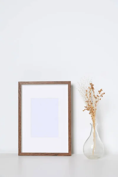 白いテーブルの上に乾燥した装飾的な花と空の写真フレームと花瓶 デザインのためのモックアップ — ストック写真