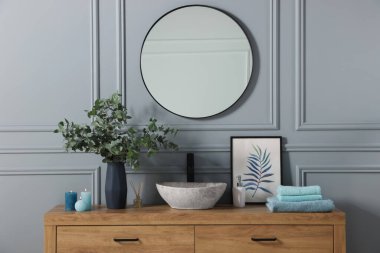 Folded towels, burning candles and eucalyptus branches near vessel sink on bathroom vanity. Interior design