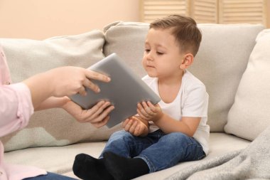 İnternet bağımlılığı. Anne, evdeki kanepede oğlunun tabletini alıp kapatıyor.