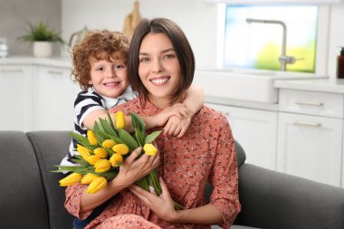 Anneler Günü 'nde annesini tebrik eden küçük bir çocuk. Sarı lale buketi tutan kadın.