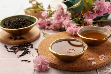 Geleneksel tören. Bir fincan demlenmiş çay, çaydanlık, kurumuş yapraklar ve kiremitli masada sakura çiçekleri, yakın plan.