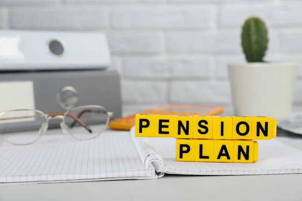Yellow cubes with phrase Pension Plan and notebook on white office table