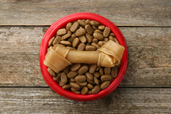 stock image Dry dog food and treat (chew bone) on wooden floor, top view