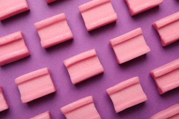 Tasty pink chewing gums on purple background, flat lay