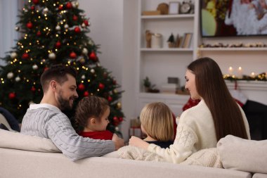 Mutlu aile TV 'nin yanındaki kanepede rahat bir odada, arka planda vakit geçiriyor. Noel atmosferi