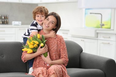 Küçük oğlu annesini Anneler Günü 'nde tebrik ediyor, mesaj için yer var. Sarı lale buketi tutan kadın.