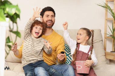 Mutlu baba ve çocuklar evdeki kanepede patlamış mısırla televizyon izliyorlar.
