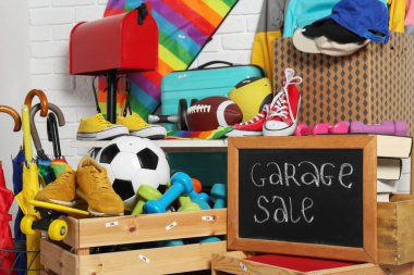Sign Garage Sale written on blackboard near many different stuff indoors