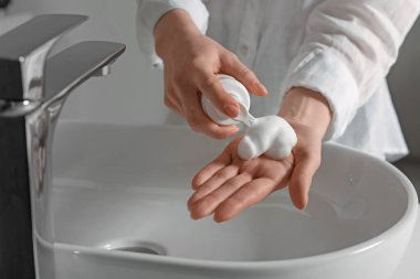 Woman washing hands with cleansing foam near sink in bathroom, closeup
