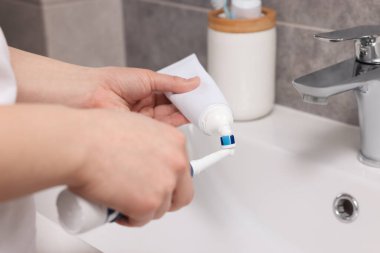 Bir kadın banyoda lavabonun üstündeki diş fırçasına diş macunu sıkıyor.