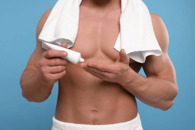 Açık mavi arka planda vücut kremi süren adam, yakın plan