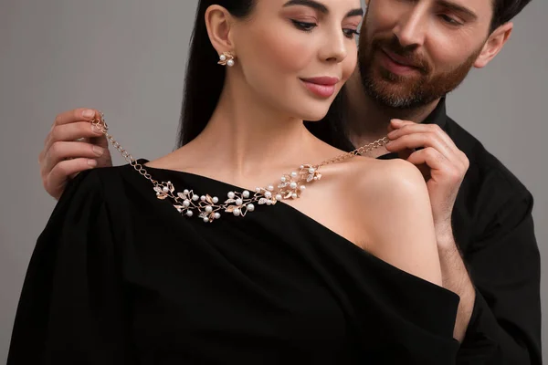 Man Sätter Elegant Halsband Vacker Kvinna Mot Grå Bakgrund Närbild — Stockfoto